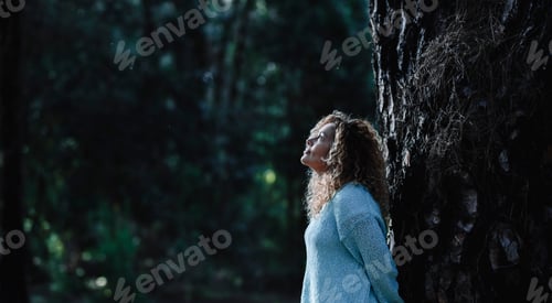 Preview: Dark image of woman standing against a tree trunk in oudoor nature leisure activity