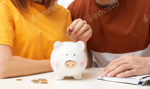 Preview: Couple putting coin into piggy bank at table, closeup. Saving money