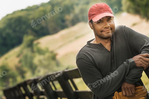 Preview: A young man with a baseball cap standing on a walkway with a rural background.