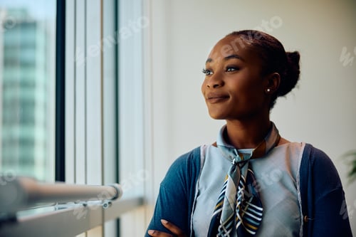 Preview: Smiling black businesswoman looking through the window of her office.