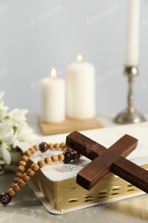 Preview: Wooden cross, Bible, rosary beads and church candles on light table, closeup