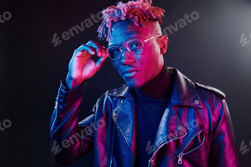Preview: Futuristic neon lighting. Young african american man in glasses standing in studio