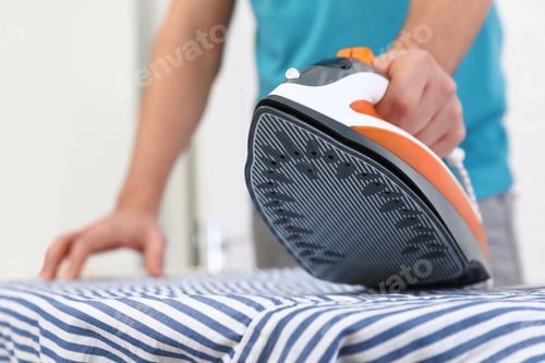 Vista previa: Man ironing shirt on board at home, closeup. Space for text