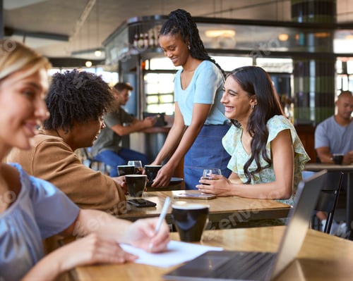 Preview: Woman Working On Laptop In Foreground With Couple Meeting Socially Behind In Busy Coffee Shop
