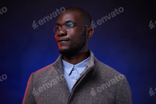Preview: Stylish African American man in gray jacket and glasses on dark background with blue light