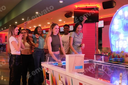 Preview: Excited friends playing air hockey and cheering in amusement arcade