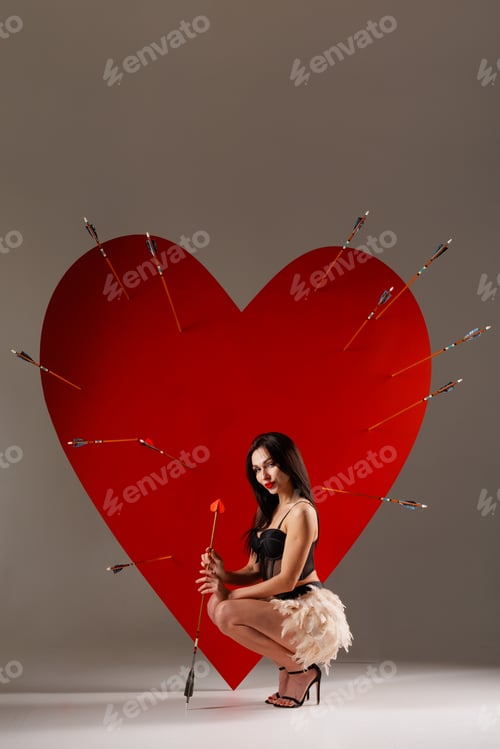 Preview: Valentine cupid woman crouching by pierced heart with arrow, studio copy space