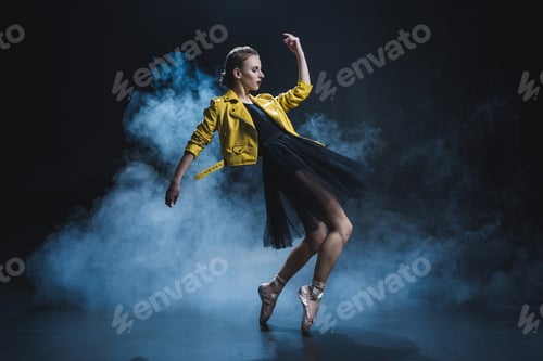 Preview: attractive girl dancing in pointe shoes and black tutu and yellow leather jacket in studio with