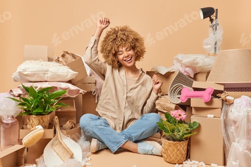 Preview: Optimistic curly haired woman wears shirt and jeans shakes arms sits crossed legs celebrates moving