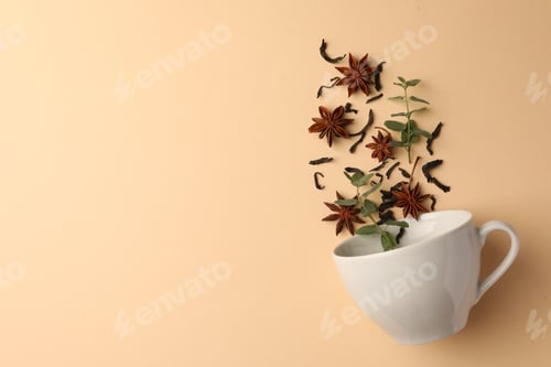 Preview: Anise stars, dry tea and mint falling into cup on beige background, flat lay. Space for text