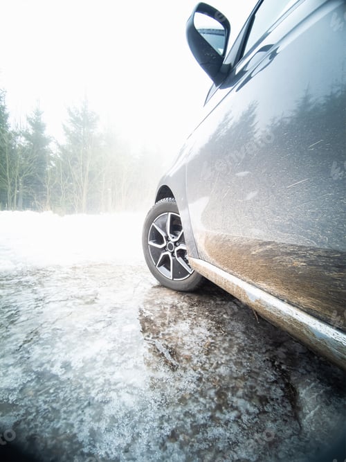 Preview: Electric car parked on a frozen puddle in the winter with a white landscape in front of it