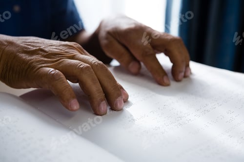 Preview: Cropped hands on retired man reading braille book in retirement home