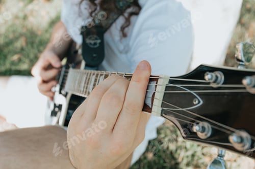 Preview: Close up of a pair of hands playing a guitar outdoors. Sunny day and practicing an instrument
