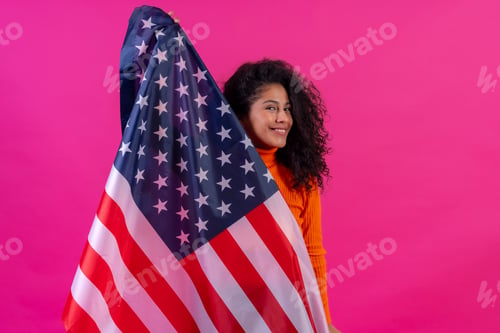 Preview: Curly-haired woman smiling with usa flag on a pink background, studio shot