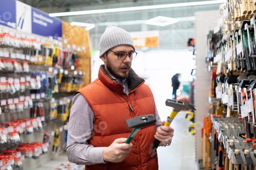 Preview: a man chooses a new hammer in a construction hypermarket