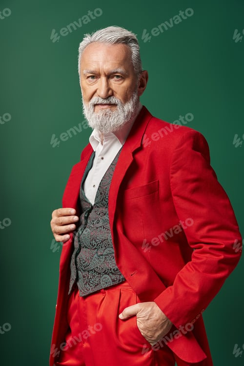 Preview: portrait of stylish Santa in elegant red suit posing with one hand in pocket, winter concept