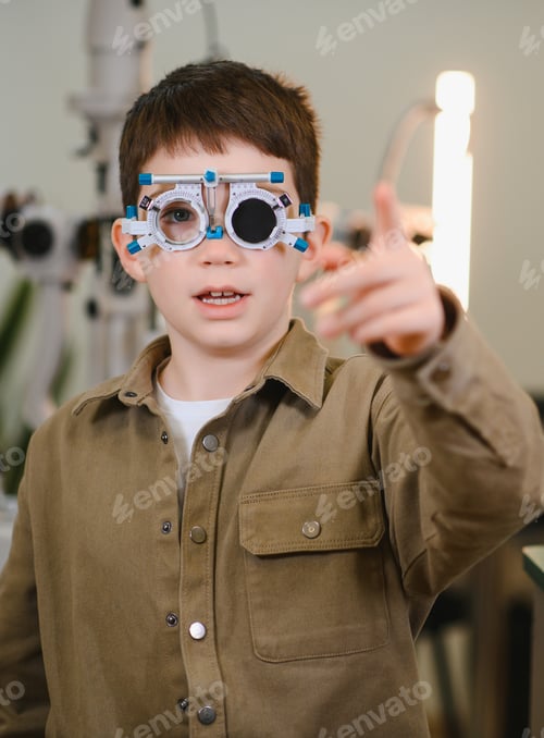 Preview: Boy undergoing eyesight examination pointing with finger at ophthalmologist cabinet