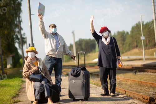 Preview: Positive elderly seniors people with face masks waiting train before traveling during a pandemic