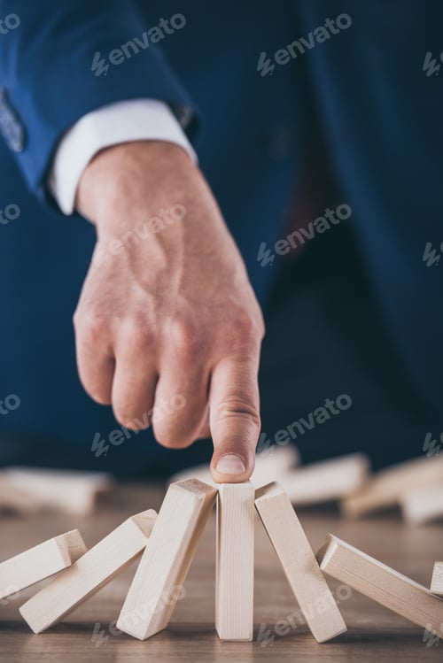 Preview: partial view of risk manager stopping domino effect of falling wooden blocks