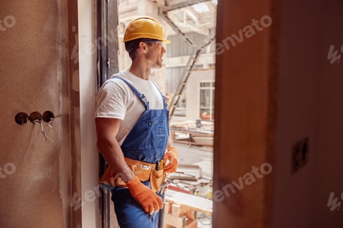 Preview: Athletic male builder in work overalls standing in doorway