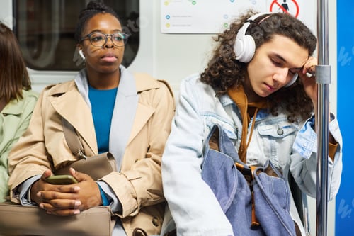 Preview: Young female passenger in earphones sitting next to teenage guy napping