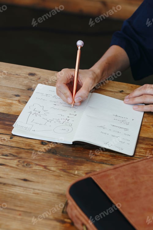 Preview: Someone jotting down ideas in a notebook at a wooden table.