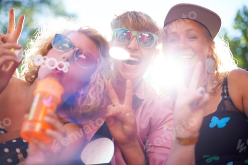 Preview: Portrait of three happy young friends standing outside and blowing bubbles