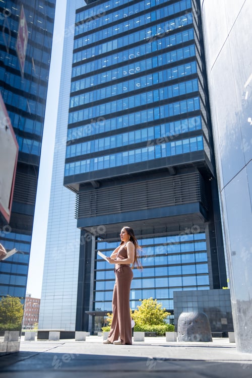 Preview: Businesswoman using tablet and talking on phone in front of modern office buildings