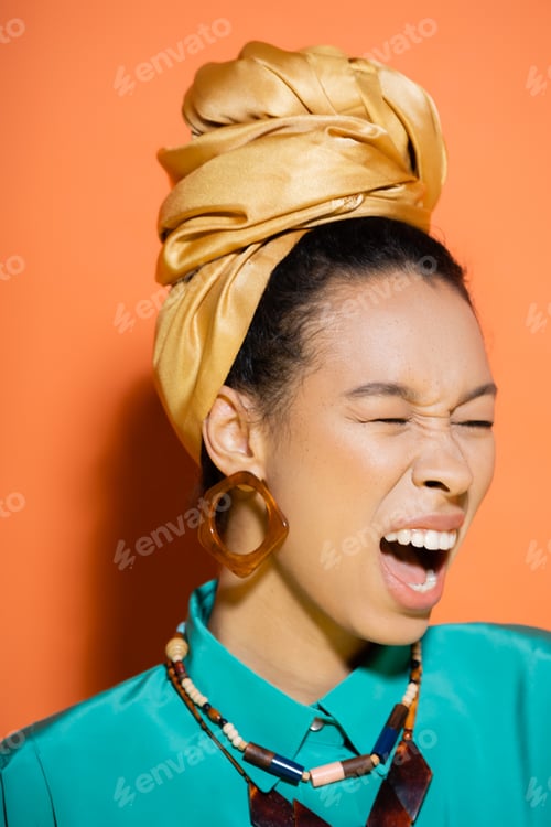 Preview: Stylish african american woman with headscarf screaming on orange background