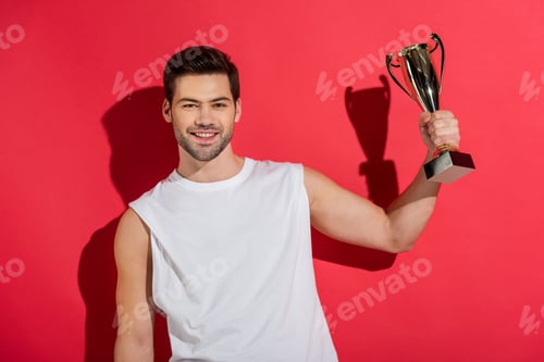 Preview: handsome young man holding trophy and smiling at camera on pink