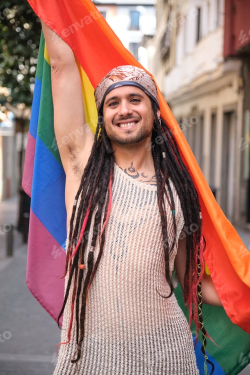 Preview: Young man with dreadlocks raising LGBT rainbow flag during pride parade