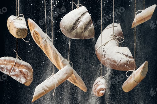 Preview: white flour falling at baked bread, baguettes and croissant hanging on ropes on black background