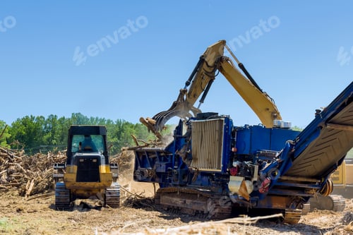 Preview: Heavy machinery operates to grind wood debris in forest clearing on sunny day