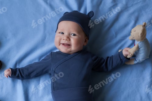 Preview: baby boy 3 months lies and smiles and holds a small toy bear in his hands.