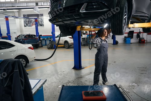 Preview: Multiracial female repairman stands under car and examines it from below