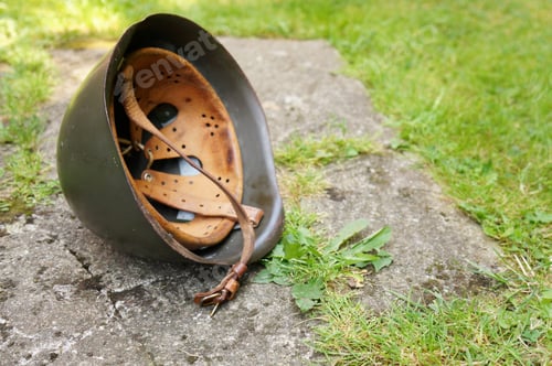 Preview: Steel helmet on the ground surrounded by the grass under the sunlight