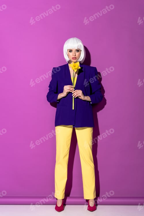 Preview: Serious girl in blue jacket holding yellow flower on purple background