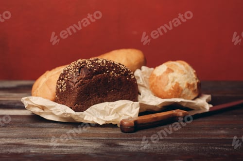 Preview: gray bread on paper packaging on wooden table and red background in the background kitchen knife