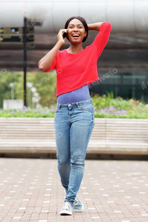Preview: Full length carefree young black woman walking with cellphone in the city