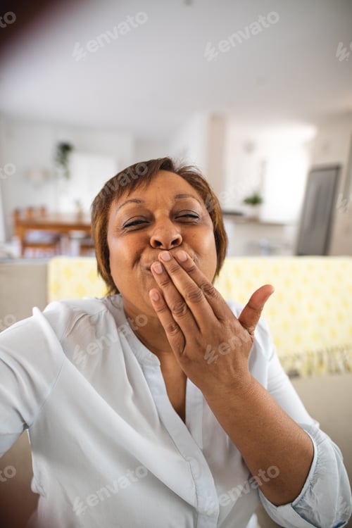 Preview: Happy african american senior woman blowing kiss during video call at home
