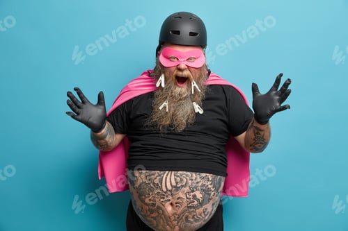 Preview: Emotional bearded man raises hands and screams loudly wears superhero costume has thick tattooed bel