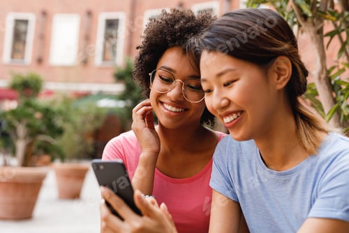Preview: Two smiling women looking at smartphone in cafe