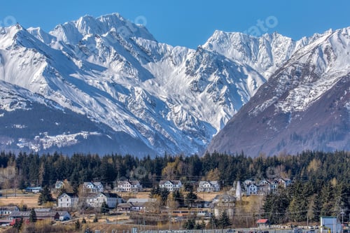 Preview: Small houses in rural field surrounded by trees and a snowy mountain in the background