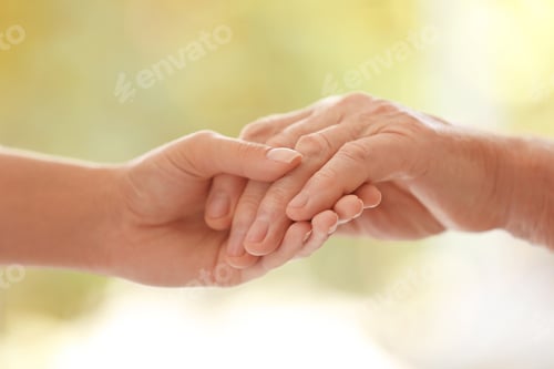 Preview: Young woman holding elderly man hand on blurred background, closeup. Help service