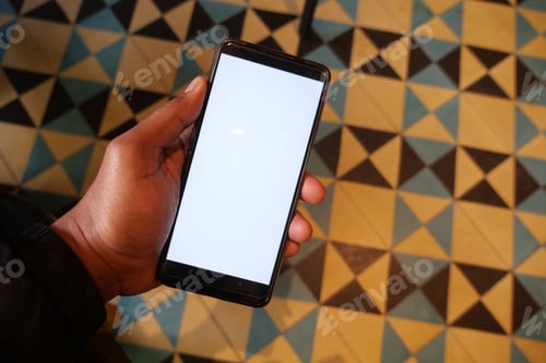 Preview: Person holding cell phone with blank screen on wooden flooring