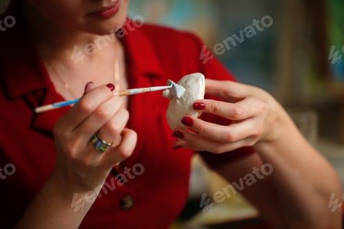 Preview: Charming Caucasian brunette woman in a red dress paints a clay cup, the concept of creativity