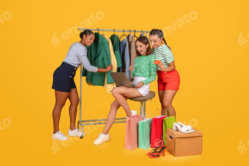 Preview: Three young ladies girlfriends shopping together online on yellow background