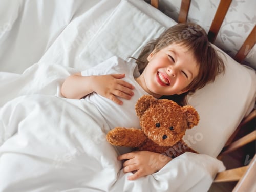 Preview: Toddler lies in bed with cute teddy bear. Little boy under white blanket with fluffy toy. Plush bear