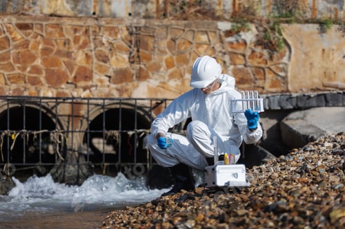 Preview: A scientist wearing a white protective suit collects and examines water samples