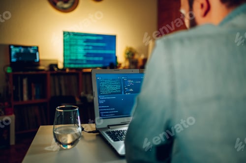 Preview: Rear view of a software engineer sitting at the home office and looking at code on a computer.
